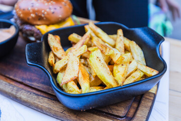 Close-up of golden-brown homestyle french fries in a black cast iron  Restaurant-quality comfort food presented on rustic wooden board.