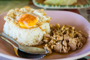 Thai dish with fried egg and pork on rice served in a pink plate with cutlery