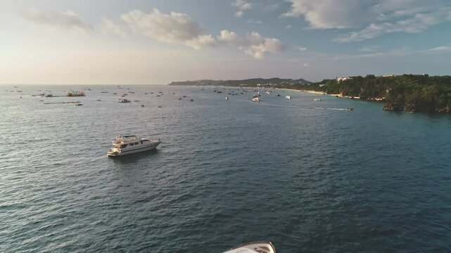 Aerial view of a luxury yacht sailing in the turquoise waters of Cagban Beach, Boracay Island, Philippines, surrounded by other boats and the coastline in the background, during a beautiful sunset