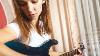 Young brunette woman playing electric guitar at home