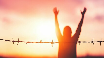 Silhouette of person celebrating freedom at sunset with barbed wire in foreground