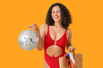 Naklejka premium Beautiful woman in swimsuit, with beach bag and disco ball on yellow background