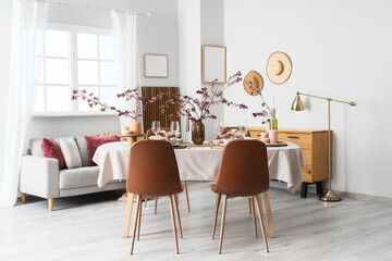 Elegant table setting with candles, plates and blooming tree branches in light living room