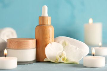 Cosmetic products, spa stones and burning candles on color table