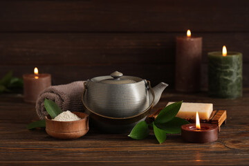 Spa composition with teapot, cosmetic products and burning candles on wooden table