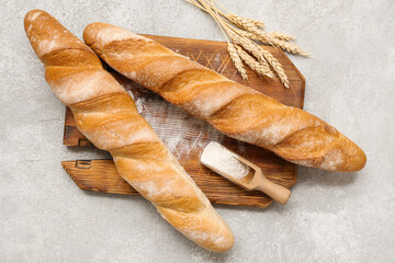 Wooden board with fresh baguettes, wheat and scoop of flour on grey background