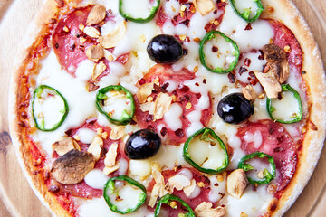 Pizza with salami and mozzarella cheese, jalapeno pepper and black olives. Wooden background. Soft focus. Close up.	
