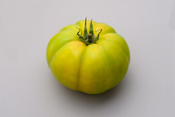 Tomato photographed on a white background, seen from above. The vegetable shows an irregular ripening with green shades. For advertising, editorial and graphic design uses.