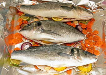 Raw sea bass and sea bream with vegetables in metal tray ready for baking