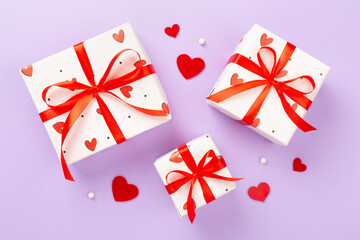 Festive gift boxes with red hearts on color background, top view