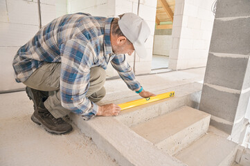 A construction worker is carefully using a level tool to ensure that the steps are perfectly aligned and stable, showcasing attention to detail in building progress