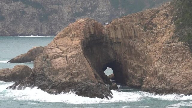 view of tourists on top of a rugged cliff surrounded by crashing waves at UNESCO Global Geopark