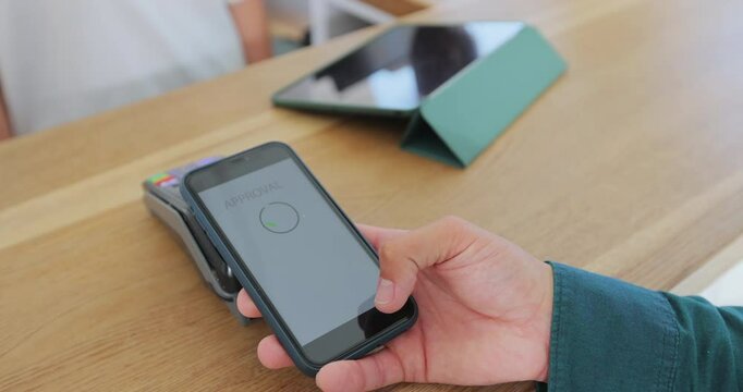Close up in the cafe woman makes coffee for a customer who pays by contactless mobile phone to credit card system.