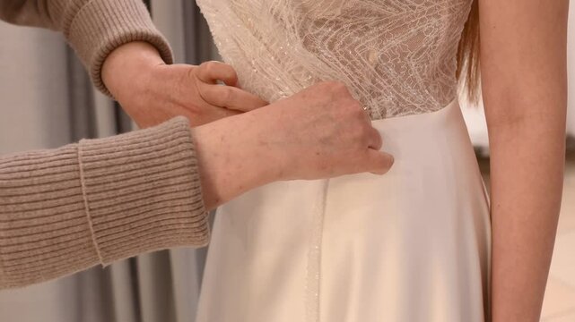 Seamstress sews lace and frill to a wedding dress on a model, mannequin. Trying on a wedding dress in a salon for custom tailoring. Basting and processing seams. closeup hands unrecognizable