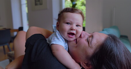 Mother kissing and cuddling baby in a warm and loving moment, with natural light streaming into a...