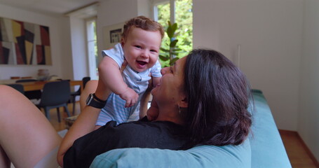 Mother kissing and cuddling baby in a warm and loving moment, with natural light streaming into a...