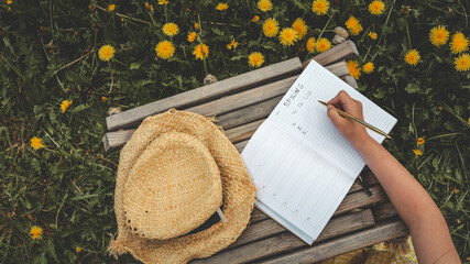 Close-up of a hand writing a spring to-do list in a lined notebook, with a background of blooming...