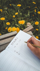 Close-up of a hand writing a spring to-do list in a lined notebook, with a background of blooming...