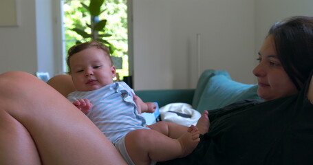 Mother lying on the sofa with baby, relaxing in a peaceful home environment, sharing quiet bonding...