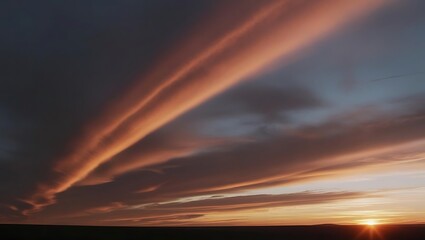 Dramatic clouds streak across a dusky sky. The setting sun casts a warm glow, contrasting with the dark expanse of the landscape below.