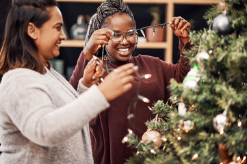 Women, people and decorate tree for Christmas, holiday spirit or cheer and festive activity for home decor. Female friends, hanging lights and bonding with celebration, happiness and xmas season.