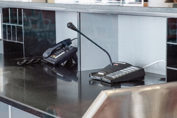 Reception desk setup with a microphone and telephone. The black countertop holds communication devices, signifying an administrative or customer service area setup