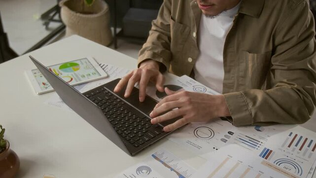 View from above of gen Z male employee dressed casually working with financial documents when making annual company report at office table