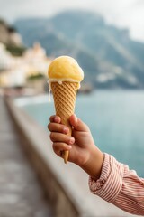 Child's hand holding a dripping cone of lemon gelato, with a medieval coastal town in soft focus behind.