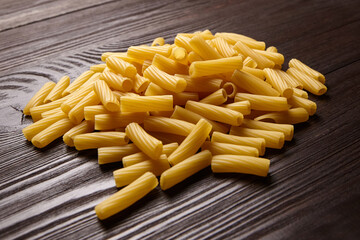 Dry yellow tortiglioni pasta pieces spread across a dark wooden surface, showing textured cylindrical shapes ideal for cooking or culinary backgrounds