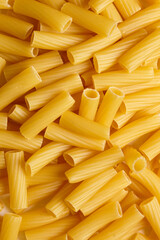 Vertical macro shot of dry tortiglioni pasta showcasing hollow ridged tubes in golden yellow, perfect for hearty Italian dishes and rustic culinary visuals