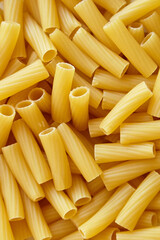Vertical close-up image of uncooked tortiglioni pasta with smooth ridges and tubular shapes, highlighting texture and golden color for food backgrounds
