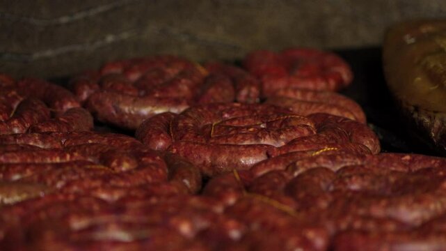 Coiled chorizos sausages release sizzling juices as they cook slowly over glowing embers on parilla grill, casings caramelizing and fat dripping, create wisps of aromatic smoke in a traditional asado