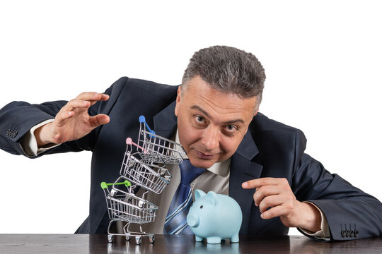 A middle-aged man in a business suit, piggy bnk  and a pyramid of empty miniature supermarket trolleys