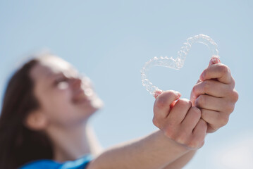 Dental care. Smiling beautiful girl holding heart-shaped aligners. Plastic retainers for teeth alignment.