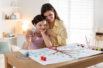 Girl and her mother drawing family tree with paints at wooden table indoors