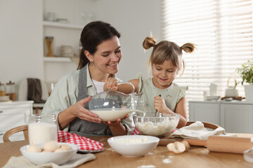 Little girl helping her mom making dough at table in kitchen