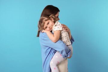 Happy mother and her cute daughter on light blue background