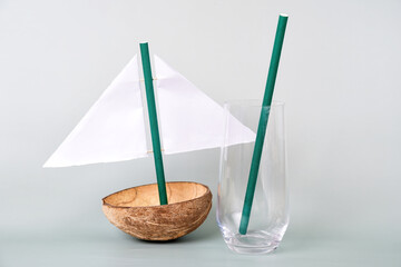 Creative sailboat made from a coconut shell and paper sail sits next to a glass with a green straw. Theme of eco-friendliness and creative reuse