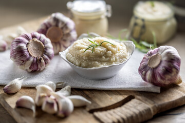 Aromatic garlic paste in a bowl laid on rustic kitchen cloth with bulbs and peeled cloves and rosemary