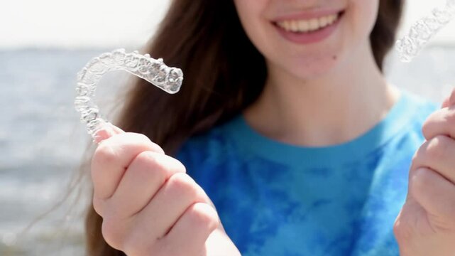 Dental care. Smiling beautiful girl holding heart-shaped aligners. Plastic retainers for teeth alignment.