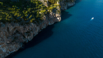 Aerial view of a rocky mountain that ends close to the blue sea. A small boat crosses the sea.