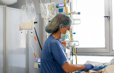 Nurse wearing surgical mask and cap preparing equipment in hospital room