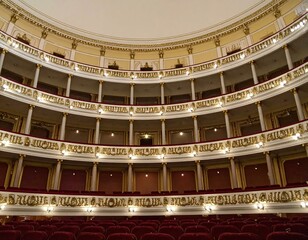 Obraz premium Elegant theater interior with ornate balconies, gold detailing, and plush red velvet seating.