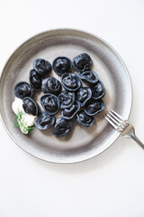 Gray Plate with Black Ravioli Dumplings, Cream and Dill. Delicious Italian or Asian Fusion Food.