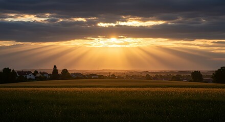 Fototapeta premium Golden Sunlight Rays Over Field Landscape and Village at Dusk