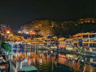 Fototapeta premium Zhangjiajie, China - Apr 07, 2025: Night scenic view of Fenghuang Ancient Town with illuminated wooden houses built on stilts over the water