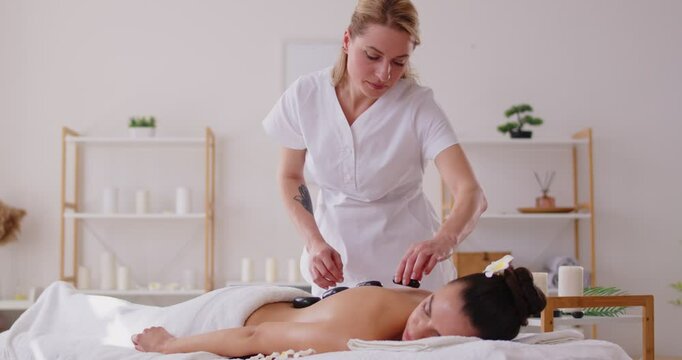 Hot stone back massage, spa and beauty salon woman cosmetologist, beautician relieves tense muscles, reduce pain, calm, pleasure, rejuvenate, relax, treatment procedure, improve female general health