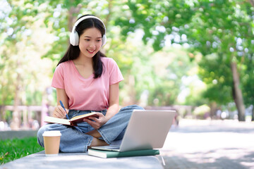Asian Young Woman Student Studying Online with Laptop and Headphones in Park Smiling Learning Note Taking Education Lifestyle