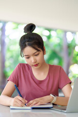 Young Asian Woman Studying Writing Notes with Laptop for Education Online Learning Homework Exam...