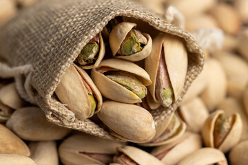 unpeeled pistachio nuts with cracked shells, poured into a coarse bag, closeup, side view